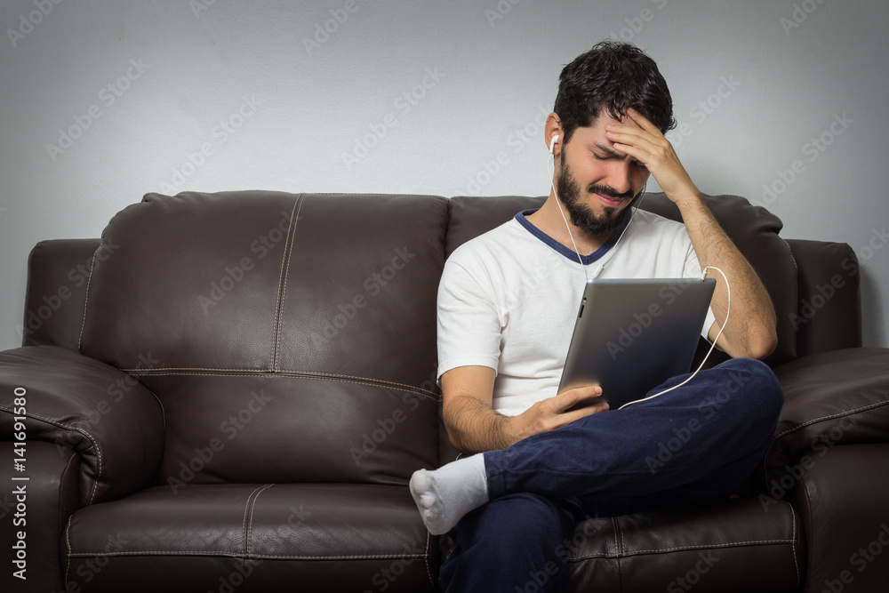 Bearded man with severe headache, worried. And looking at tablet. Bad news concept.