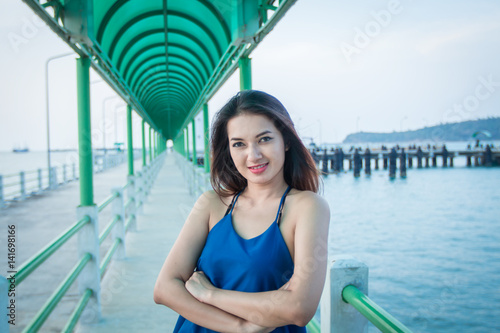 Portrait of Asian woman with arms crossed smiling outside by the sea.