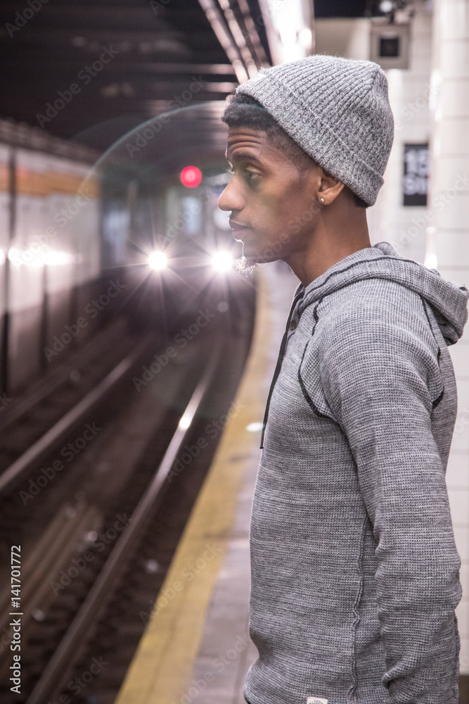 A young, black hipster waits for a NYC subway train