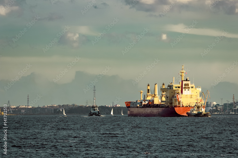 Red cargo ship and the tug ship towing it to the port Red cargo ship and the tug ship towing it to the port