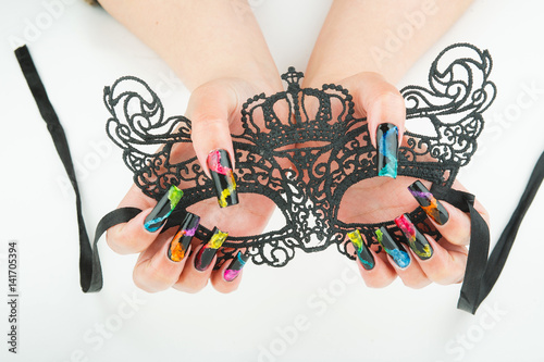 hands with beautiful manicure holding a black lace carnival mask on white background