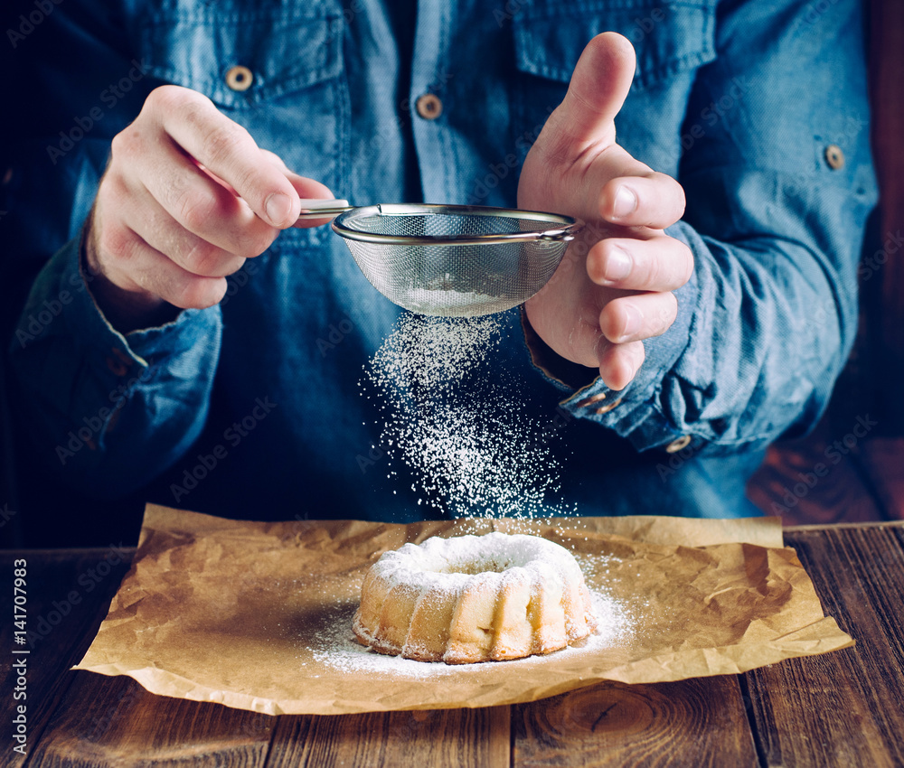 Fototapeta premium Hands sprinkling with icing sugar ring cake