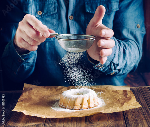 Hands sprinkling with icing sugar ring cake