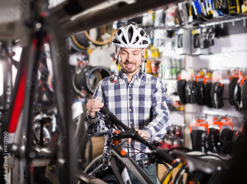 attentive man in helmet chooses for himself sports bike in bicycle shop