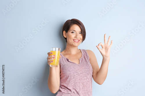Young beautiful woman with glass of orange juice, on light background