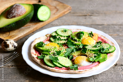 Homemade tortilla with fried quail eggs, avocado, cucumber, beet hummus and parsley. Quick and easy breakfast tortilla on a plate and on vintage wooden table. Healthy food idea