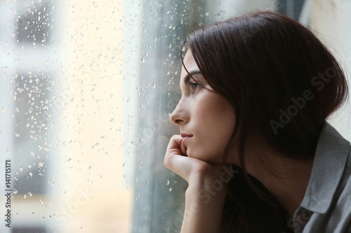 Fototapeta Depressed young woman near window at home, closeup