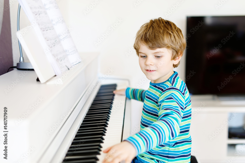 Fototapeta Beautiful little kid boy playing piano in living room or music school