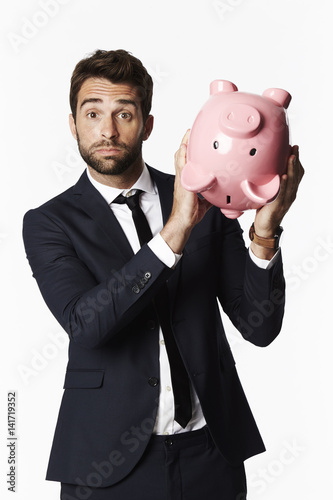 Businessman holding piggybank upside down, portrait