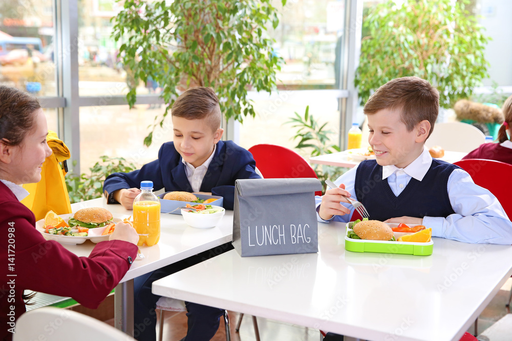 Children sitting at cafeteria table while eating lunch Stock Photo ...