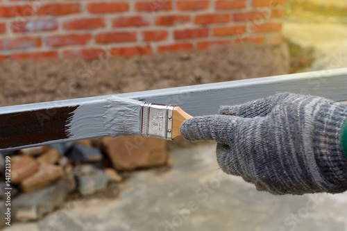 Gloved hand painting primer anti rust on steel poles for construction. Half - painted surface. Smear of paint brush. photo