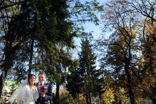 Cheerful wedding couple with violet bouquet stands in bright autumn park