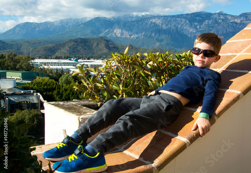 Мальчик ледит на краю террасы, с которой открывается прекрасный вид на горы