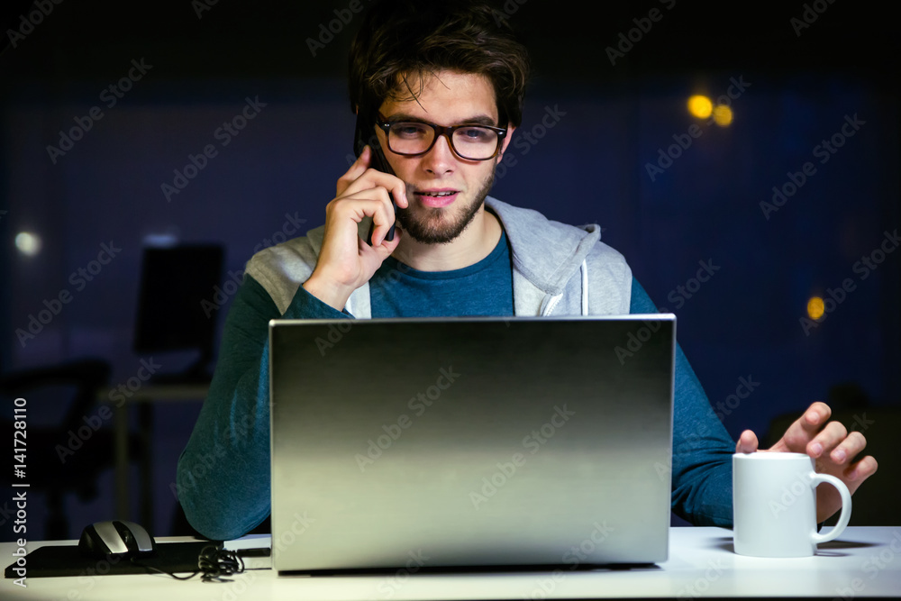 Handsome young man working with laptop in his office at night. Handsome young man working with laptop in his office at night.