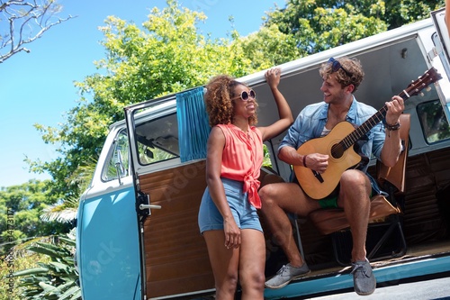 Man playing guitar in campervan and woman standing beside him