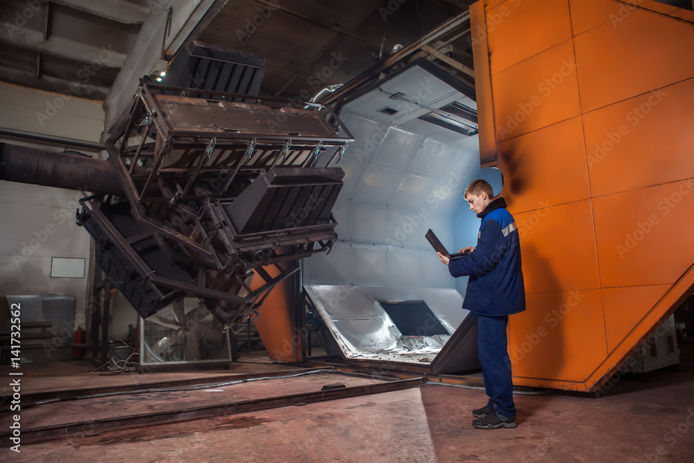 Molding plastics in the huge factory oven. Worker with the laptop is