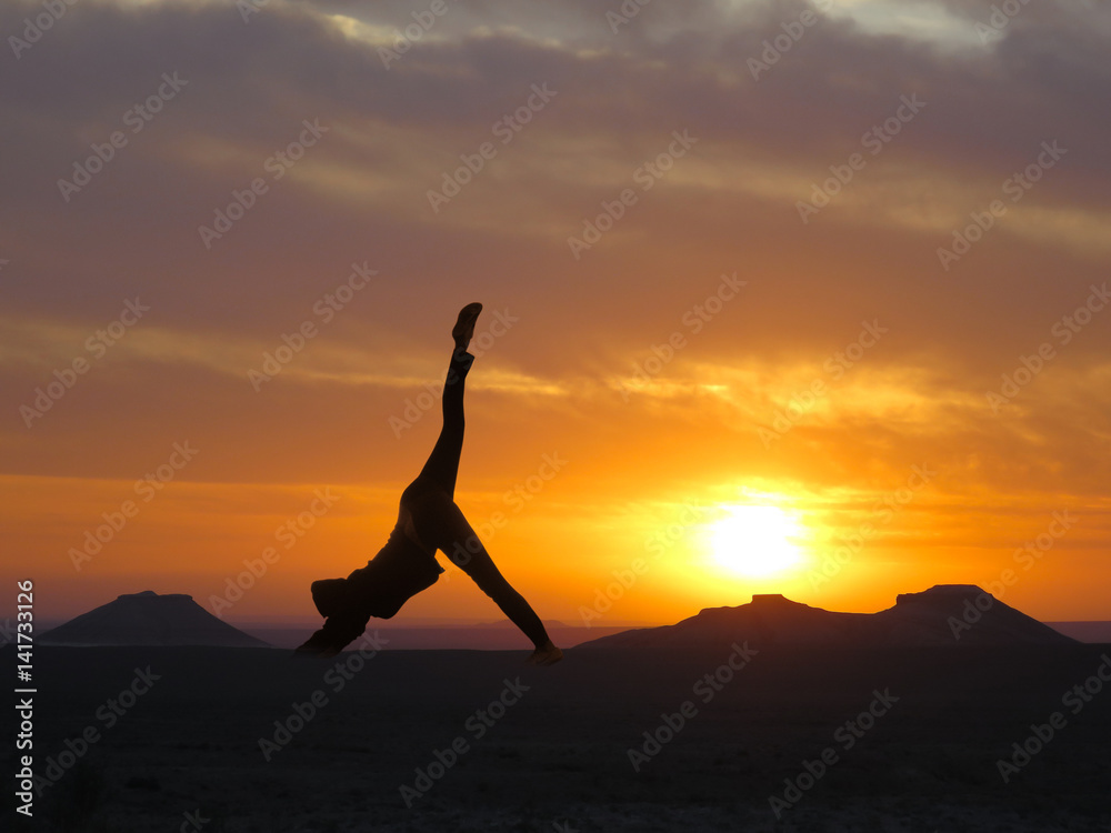 Girl practicing yoga on a background of mountains and sunset