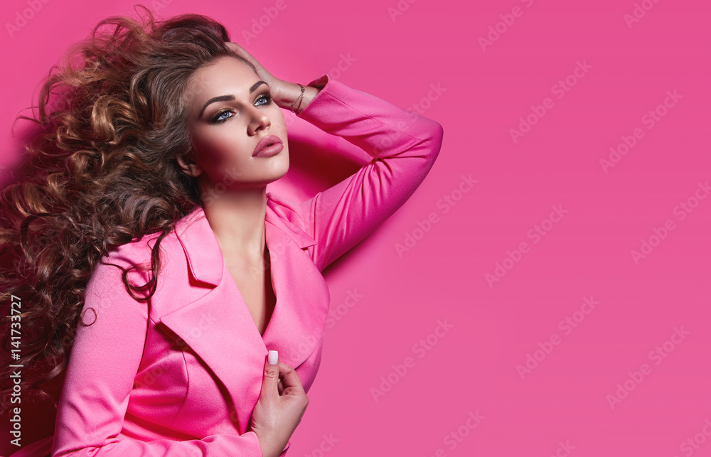 Beautiful fashionable girl haired with long curly hair in a pink jacket. The girl in the studio on a pink background. - obrazy, fototapety, plakaty 