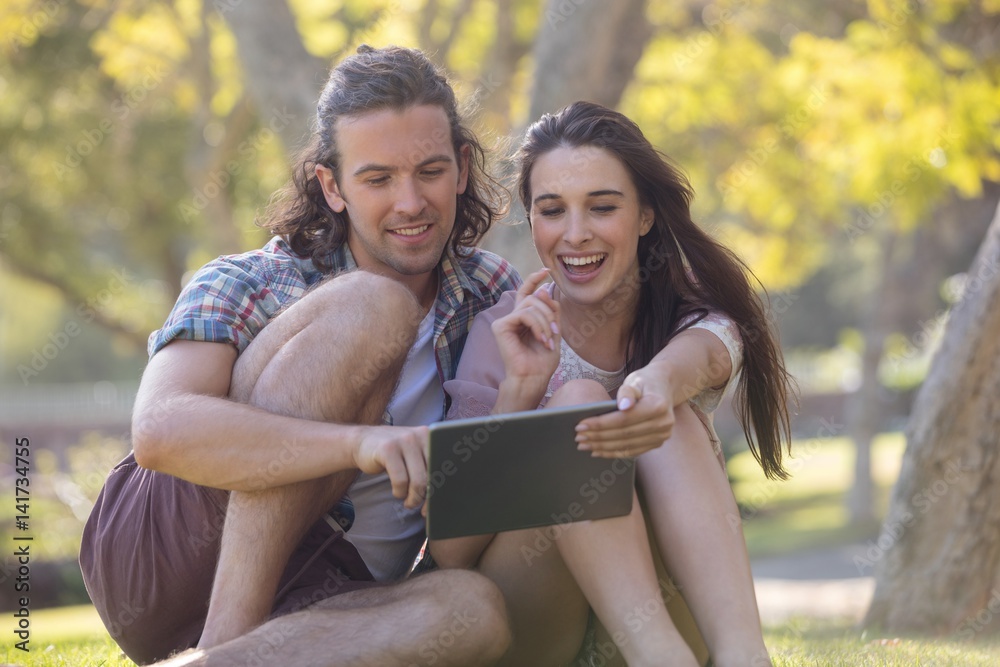 Couple sitting on grass and using digital tablet Couple sitting on grass and using digital tablet