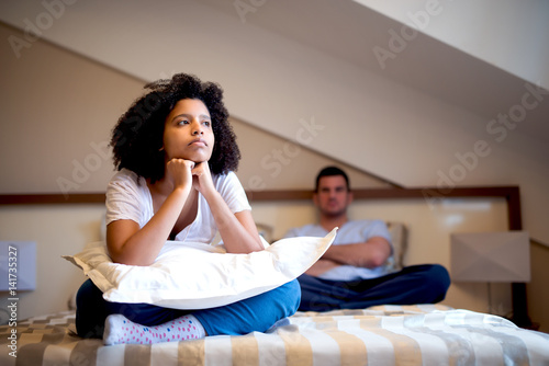 Unhappy couple sitting on bed after argument. Looking sad and annoyed. photo