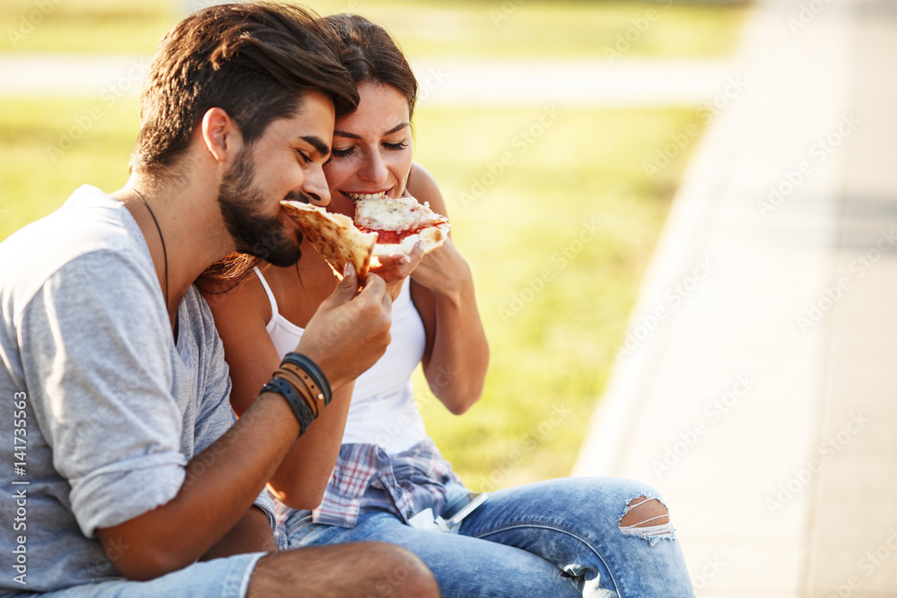 Young couple sitting on a park bench and eating pizza. Fast food. Young couple sitting on a park bench and eating pizza. Fast food.
