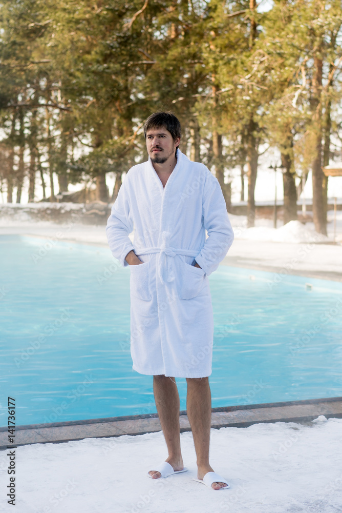 Young man in bathrobe near outdoor swimming pool at winter day Young man in bathrobe near outdoor swimming pool at winter day