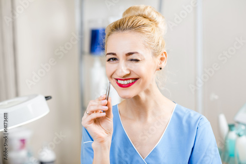 Portrait of female cosmetologist in uniform holding tweezers in the cosmetology office