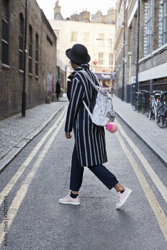 Side view of woman in hat and striped coat walking in street