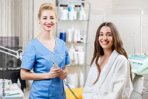 Portrait of female cosmetologist with young woman client in bathrobe sitting in the cosmetologist office