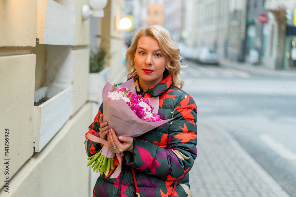 Young blonde woman with flowers bouquet on a city street at cloudy day Young blonde woman with flowers bouquet on a city street at cloudy day