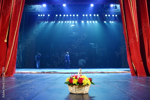 wicker basket with flowers standing on the stage.on the background of red theater curtain