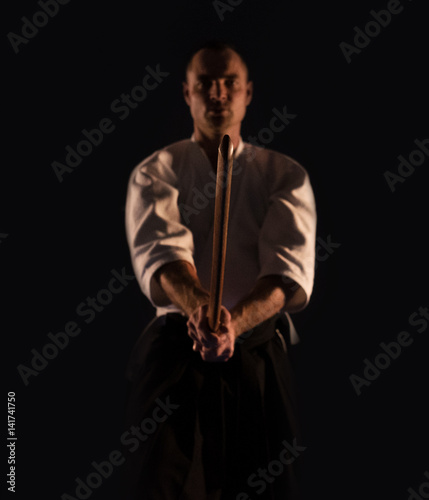 Aikido practicer (Aikidoka) with a training wooden sword (boken) dark dojo photo