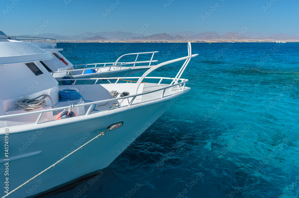 View at the coral sea and white yacht. Perfect place for snorkeling. Summer vacation at sea with turquoise clear water.