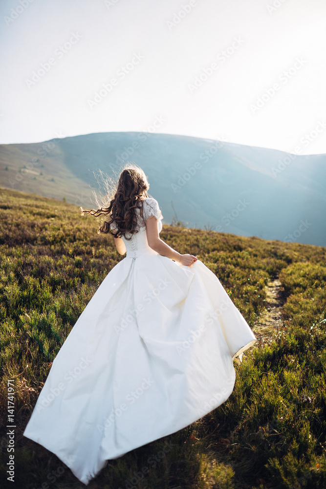 Bride in dress with long train runs across the hill to the sun