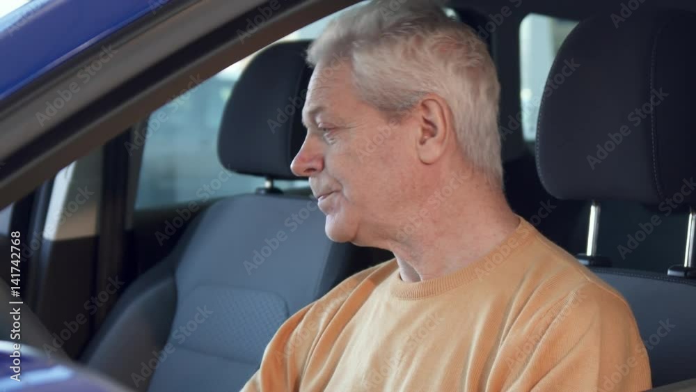 Attractive senior man showing car key though the window. Gray male customer sticking his hand out of the vehicle. Close up of aged caucasian client sitting on the driver's seat Attractive senior man showing car key though the window. Gray male customer sticking his hand out of the vehicle. Close up of aged caucasian client sitting on the driver's seat