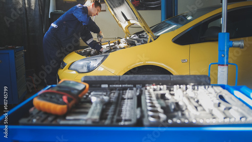 Car auto electronics - mechanic repairs a car - unscrews detail of automobile - garage service