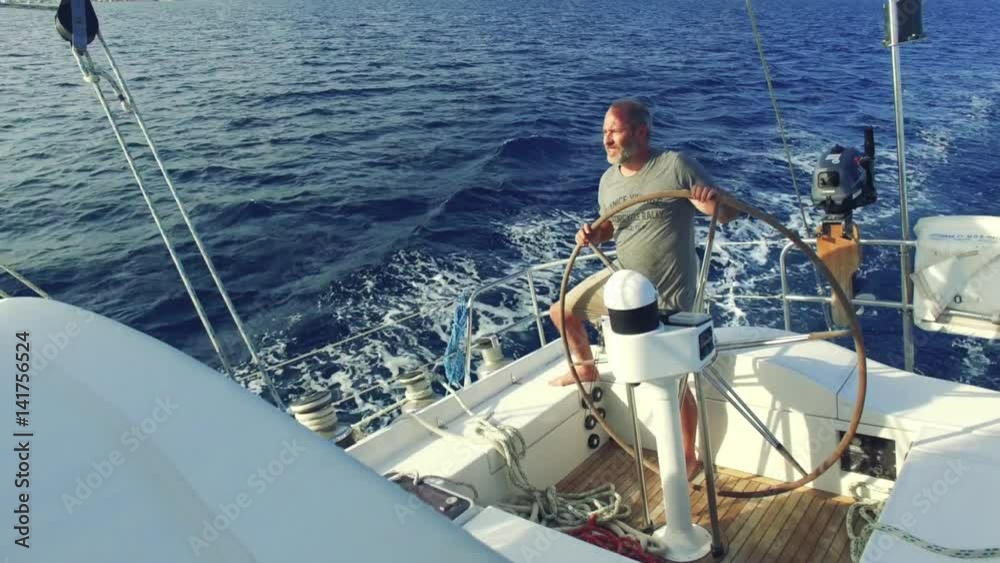man on steering wheel navigating sail boat