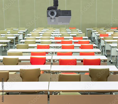 A projector over empty seats with tables in a conference hall. photo