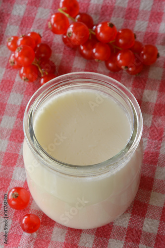 yogurt in a jar with red currant berries on a gingham tablecloth