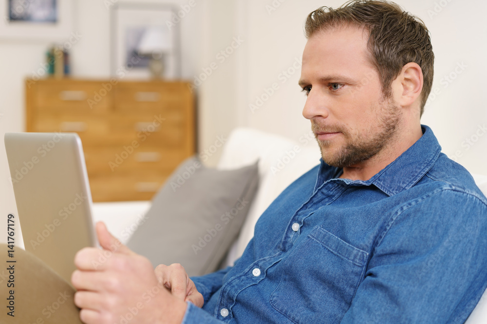mann sitzt zuhause auf dem sofa und schaut mit ernstem gesicht auf sein notebook mann sitzt zuhause auf dem sofa und schaut mit ernstem gesicht auf sein notebook