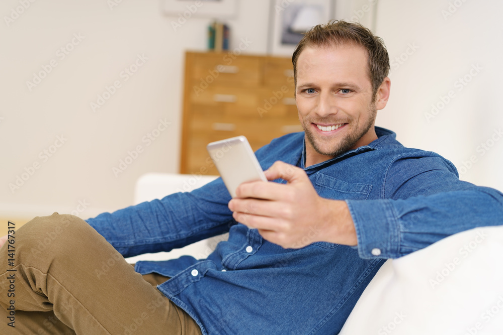 glücklicher mann sitzt entspannt auf dem sofa und hält sein mobiltelefon in der hand glücklicher mann sitzt entspannt auf dem sofa und hält sein mobiltelefon in der hand