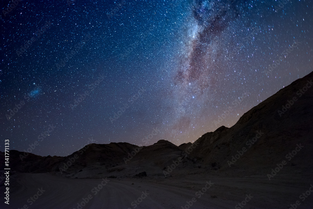 Starry sky and Milky Way arc, with details of its colorful core, outstandingly bright, captured from the Namib desert in Namibia, Africa. The Small Magellanic Cloud on the left hand side. - obrazy, fototapety, plakaty 