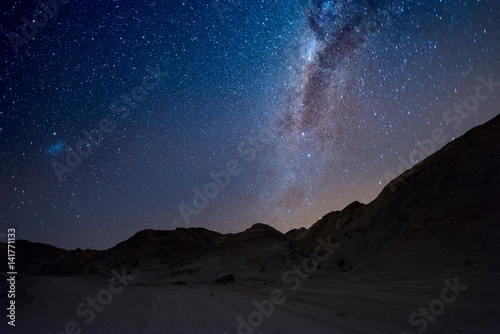 Starry sky and Milky Way arc, with details of its colorful core, outstandingly bright, captured from the Namib desert in Namibia, Africa. The Small Magellanic Cloud on the left hand side.