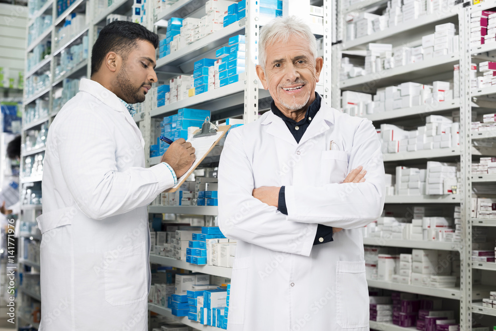 Senior Chemist Standing Arms Crossed While Colleague Counting St Senior Chemist Standing Arms Crossed While Colleague Counting St