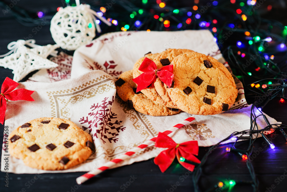 Winter, New Year's atmosphere, American vanilla cookies with chocolate and a glass of milk on a background of colored garlands 