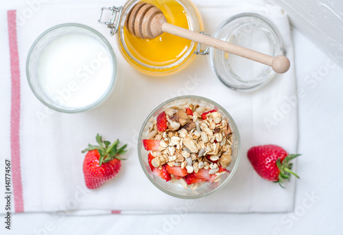 Top view healthy breakfast of homemade granola cereal with milk, strawberry, nuts and fruit, honey with drizzlier on white background. Morning food, Diet, Detox, Clean Eating, Vegetarian concept. photo