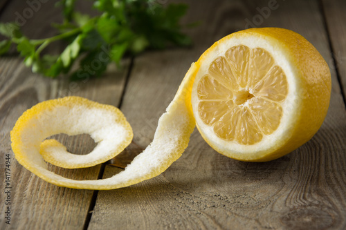 Half peeled fresh lemon on a wooden table with green herbs in the background