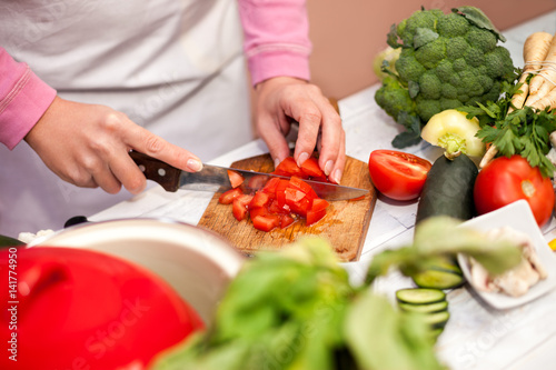 Cutting tomato with knife, preparing vegetable for salad