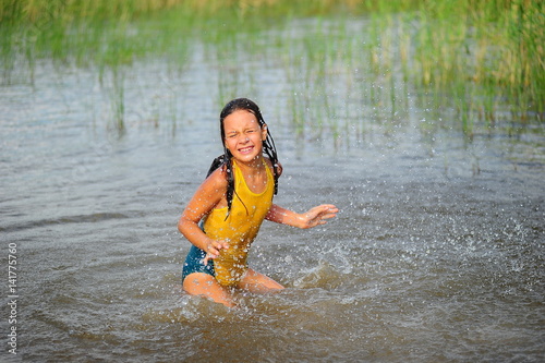 Fototapeta Naklejka Na Ścianę i Meble -  Little girl in a yellow bathing suit playing in the water