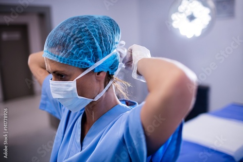 Female nurse tying surgical mask in operation theater photo